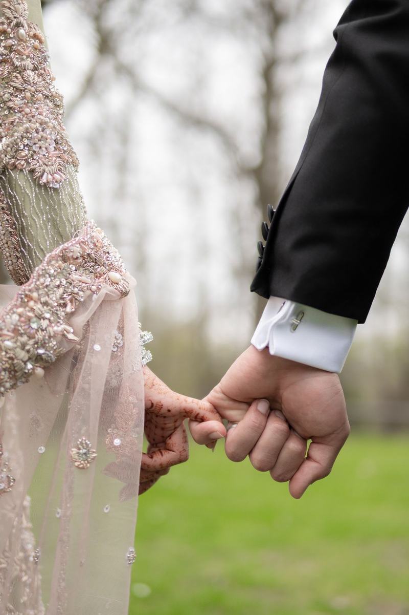 Close up of bride and groom holding hands with henna detail