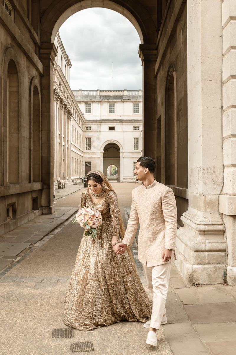 Bride and groom walking hand in hand through a stone archway