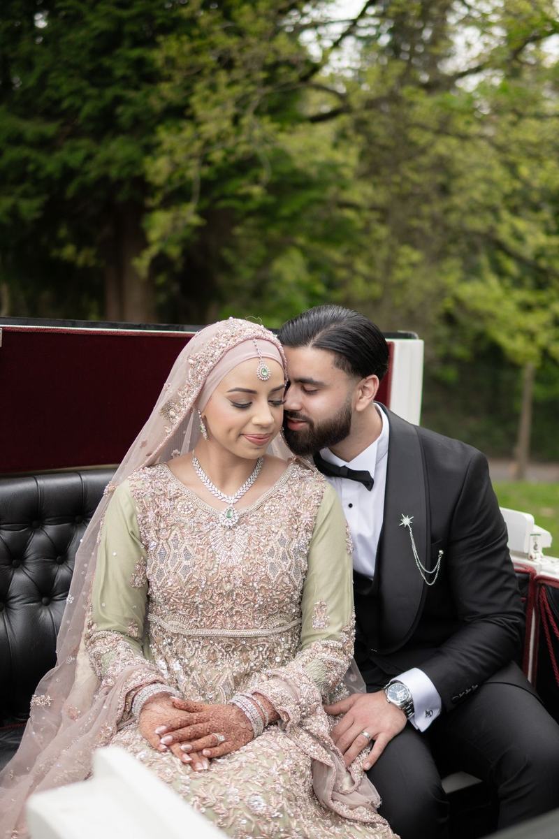 Groom nuzzling bride in horse-drawn carriage