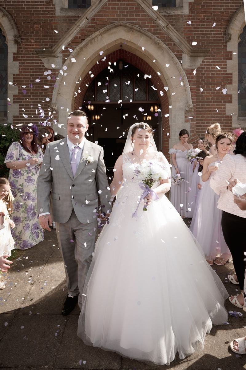 Bride and groom walking through confetti outside a church