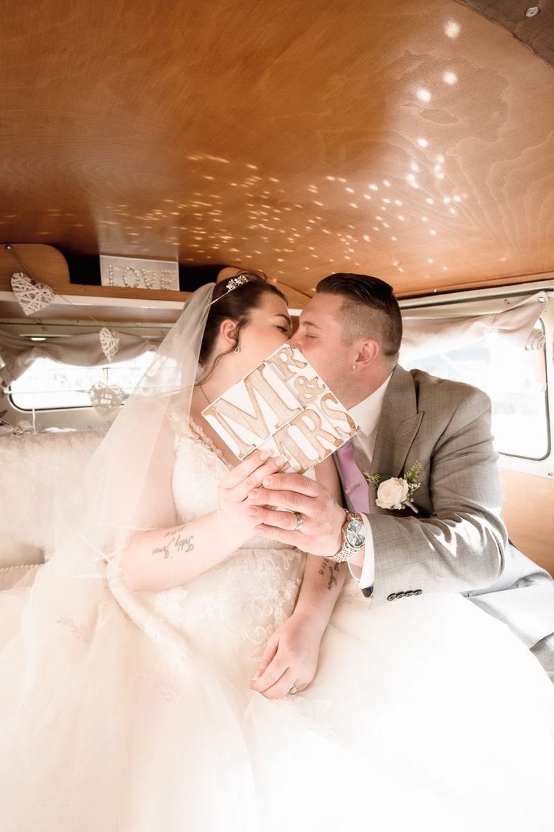 Bride and groom kissing behind a Mr and Mrs sign inside a VW van