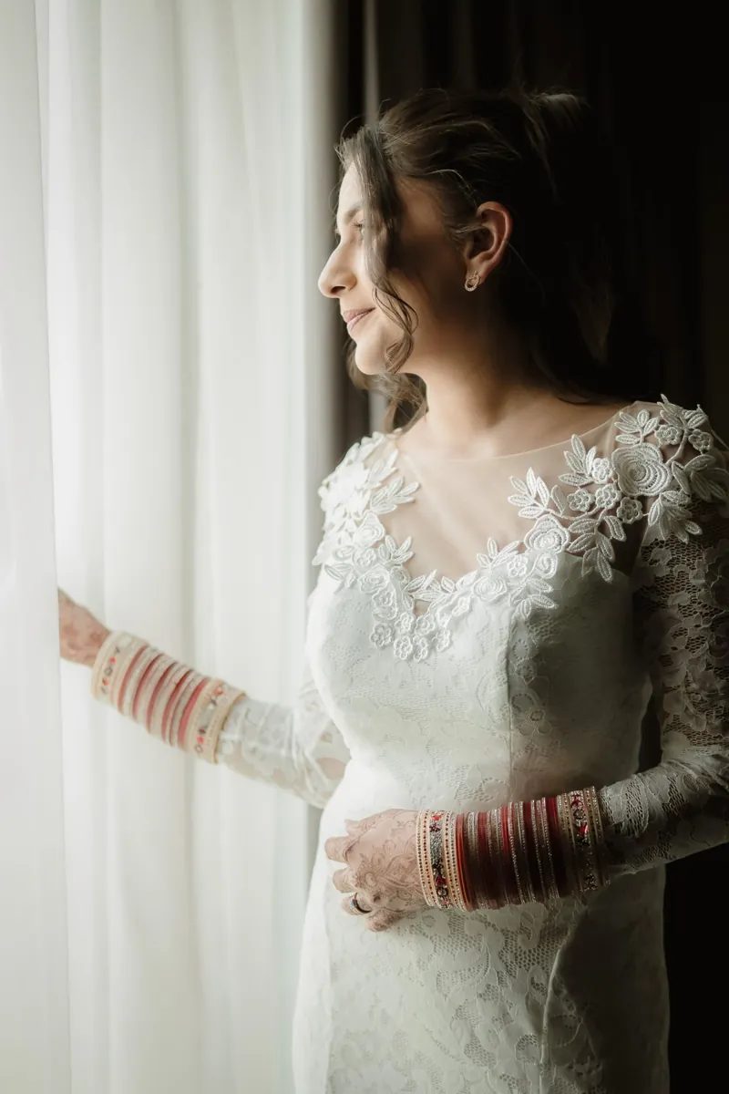 Bride in a lace wedding dress looking out of a window