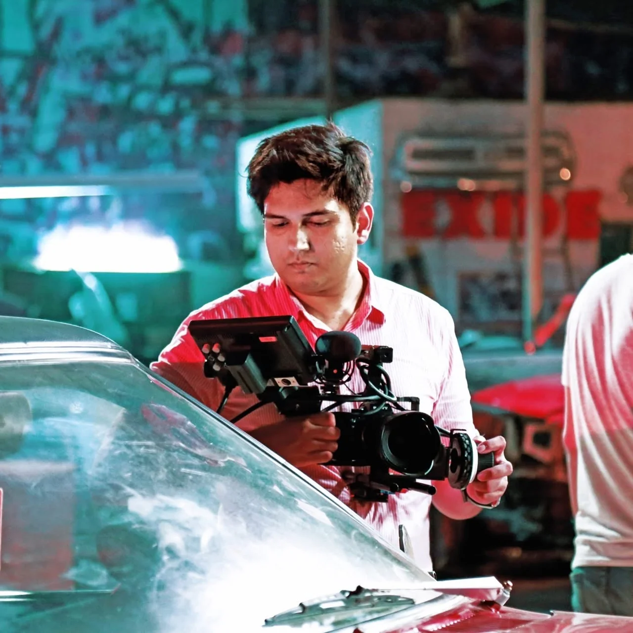 Moiz filming behind the scenes with a cinema camera beside a car on a feature film set