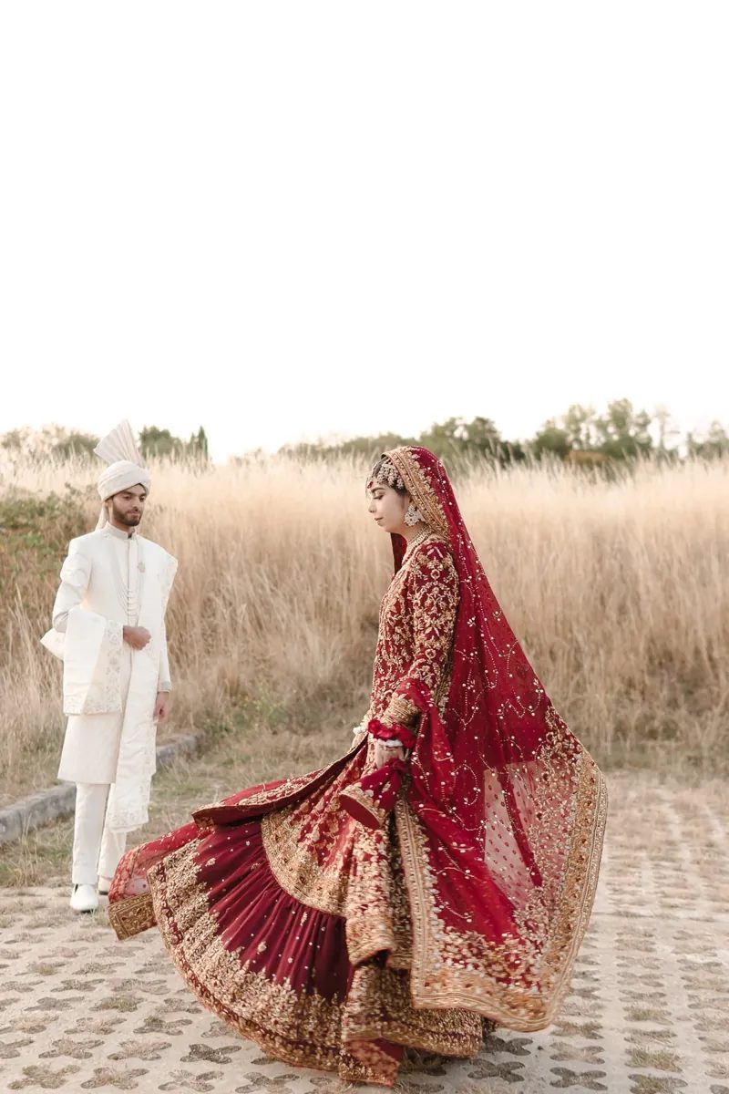 Bride twirling her red and gold lehenga as the groom watches