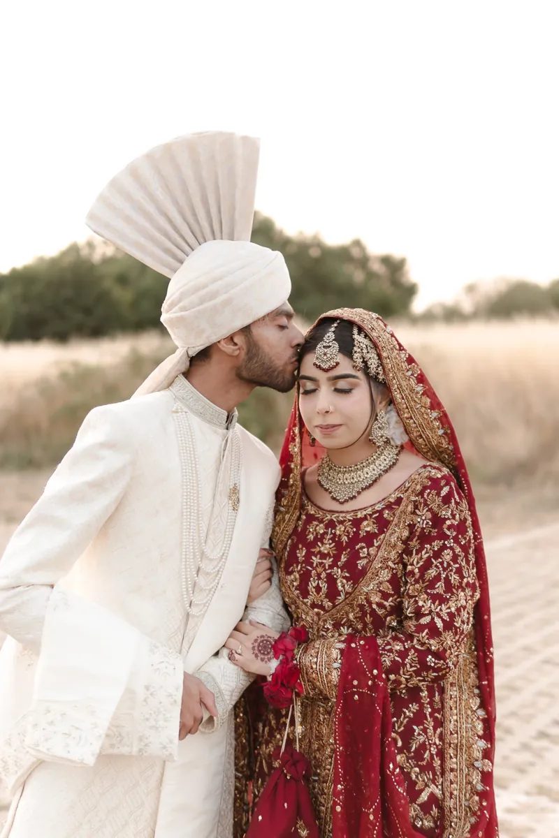 Groom in an ivory turban kissing the bride's forehead