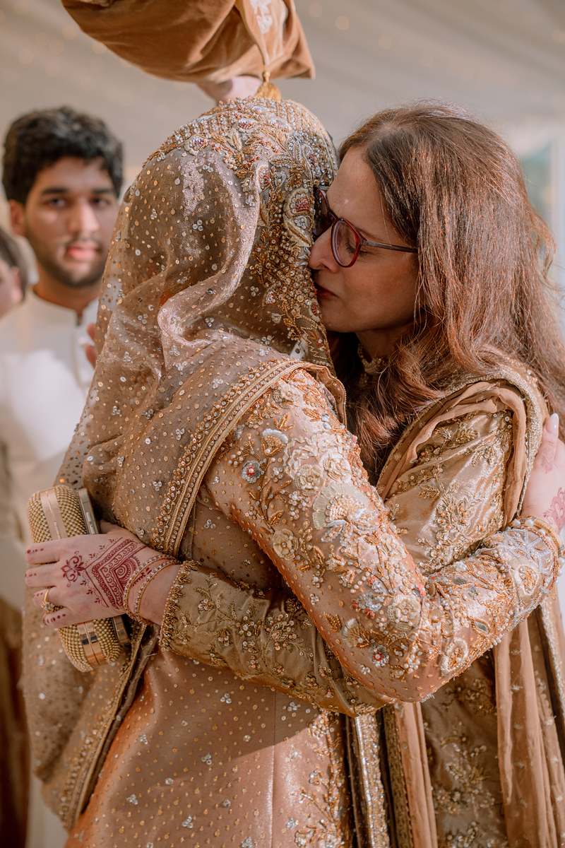 The bride held close by her mother beneath the Quran