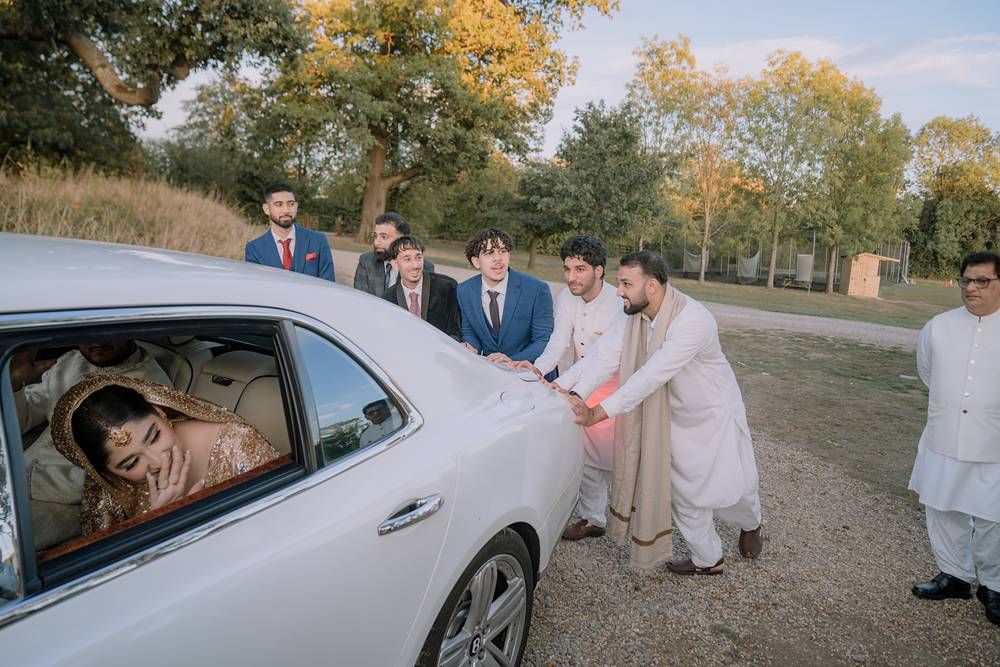 The groom’s friends push the bridal car as the bride laughs