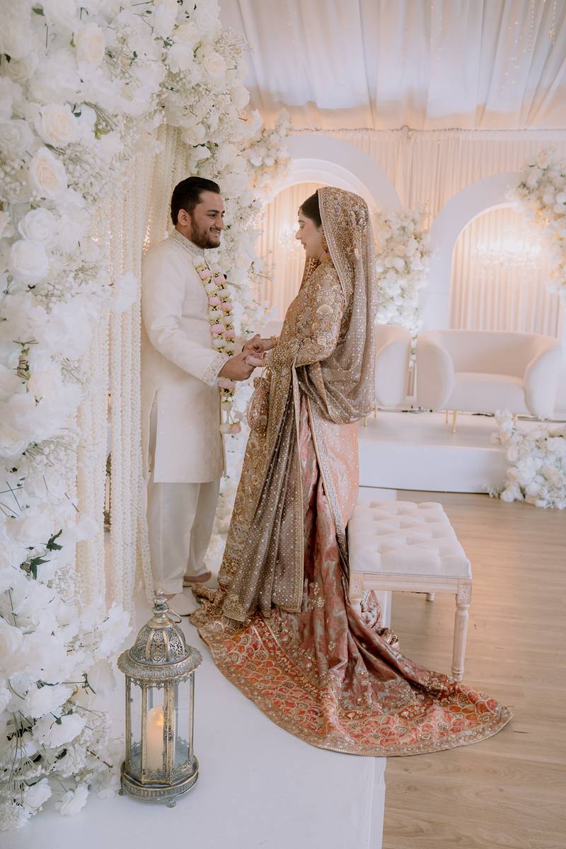 Hand in hand at the white floral Nikah stage