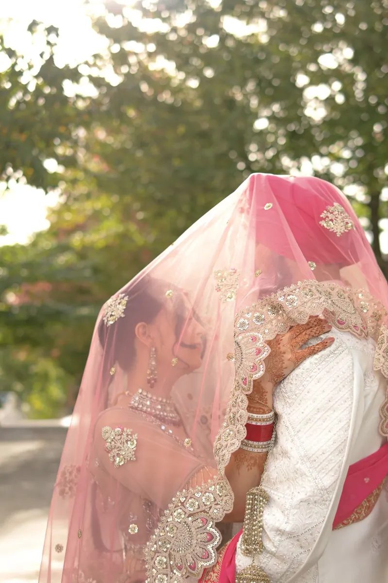 Bride and groom embracing beneath a sheer pink dupatta