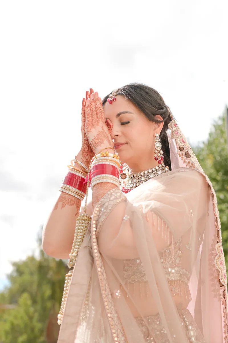Bride with hands pressed together in prayer, wearing red chooda and henna