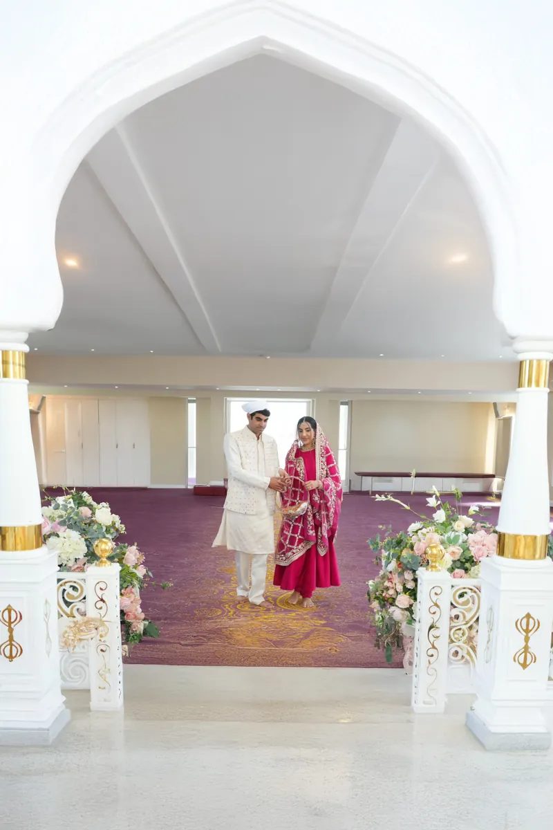 Bride and groom walking through the Gurdwara beneath a white arch