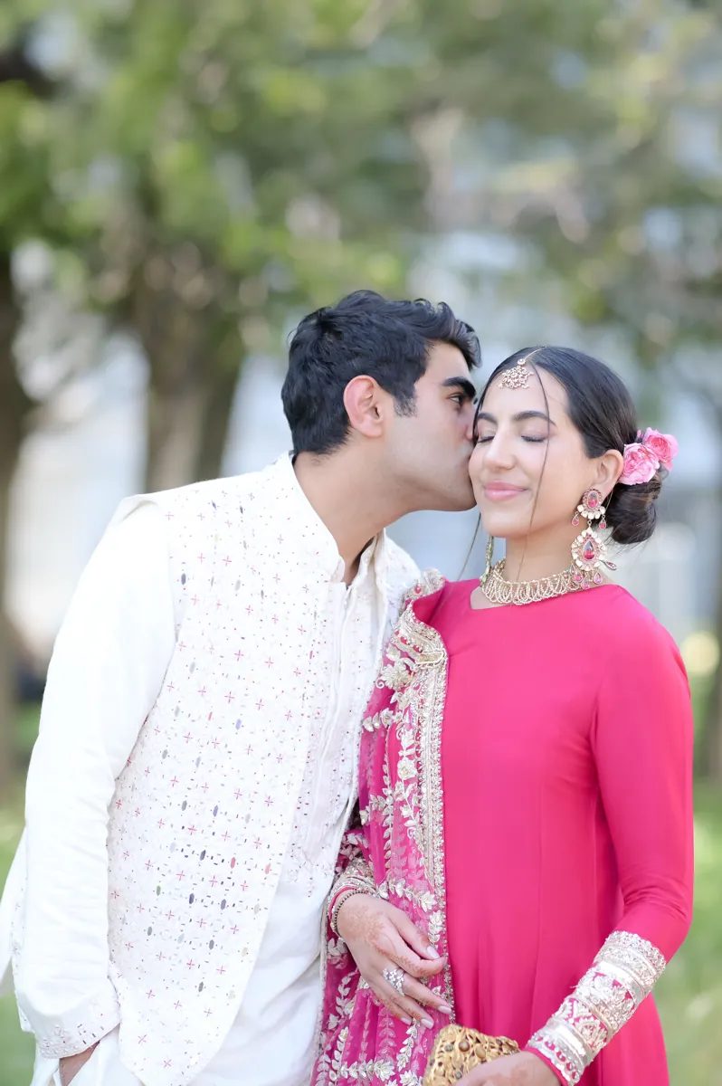 Groom kissing the bride's cheek under the trees