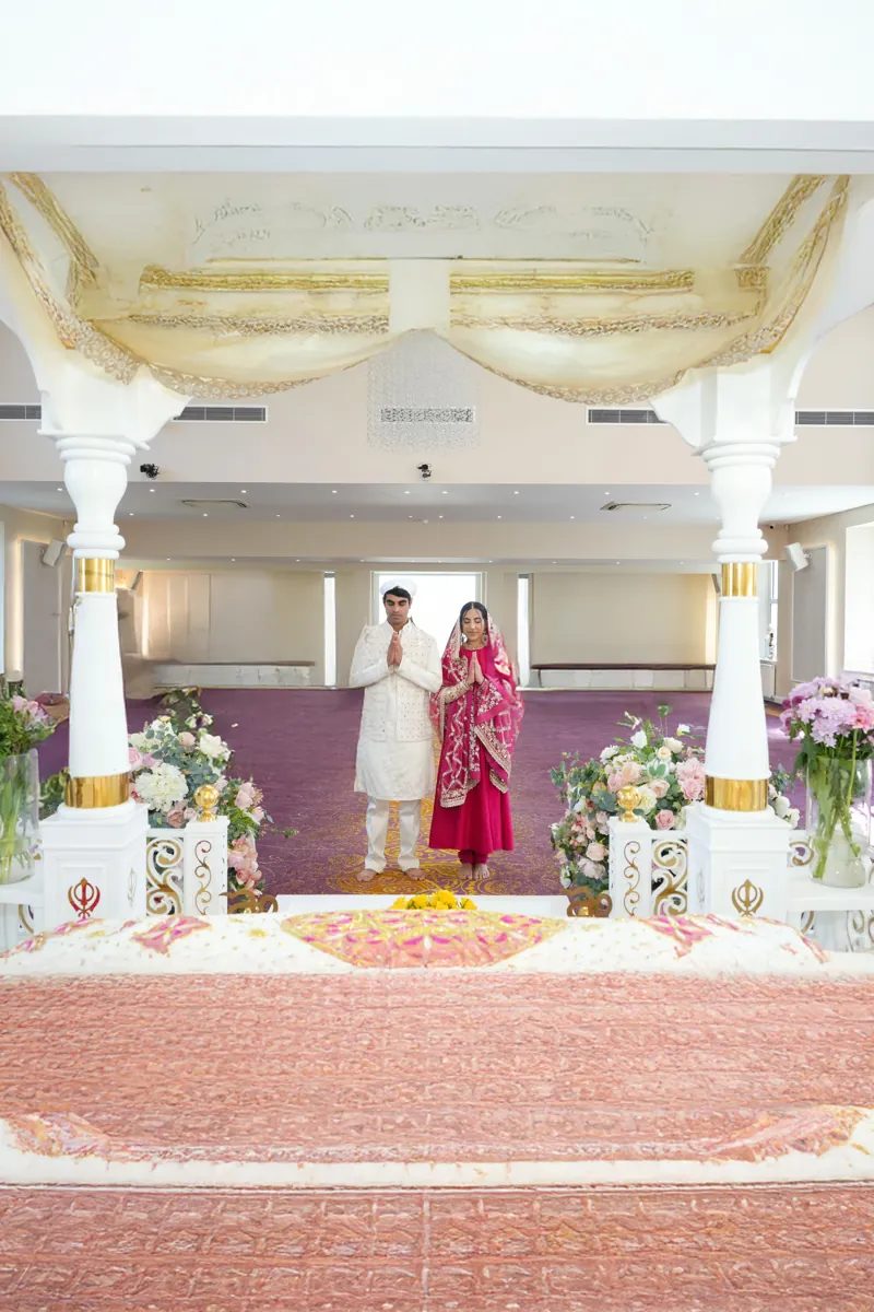Bride and groom with hands pressed together inside the Gurdwara prayer hall
