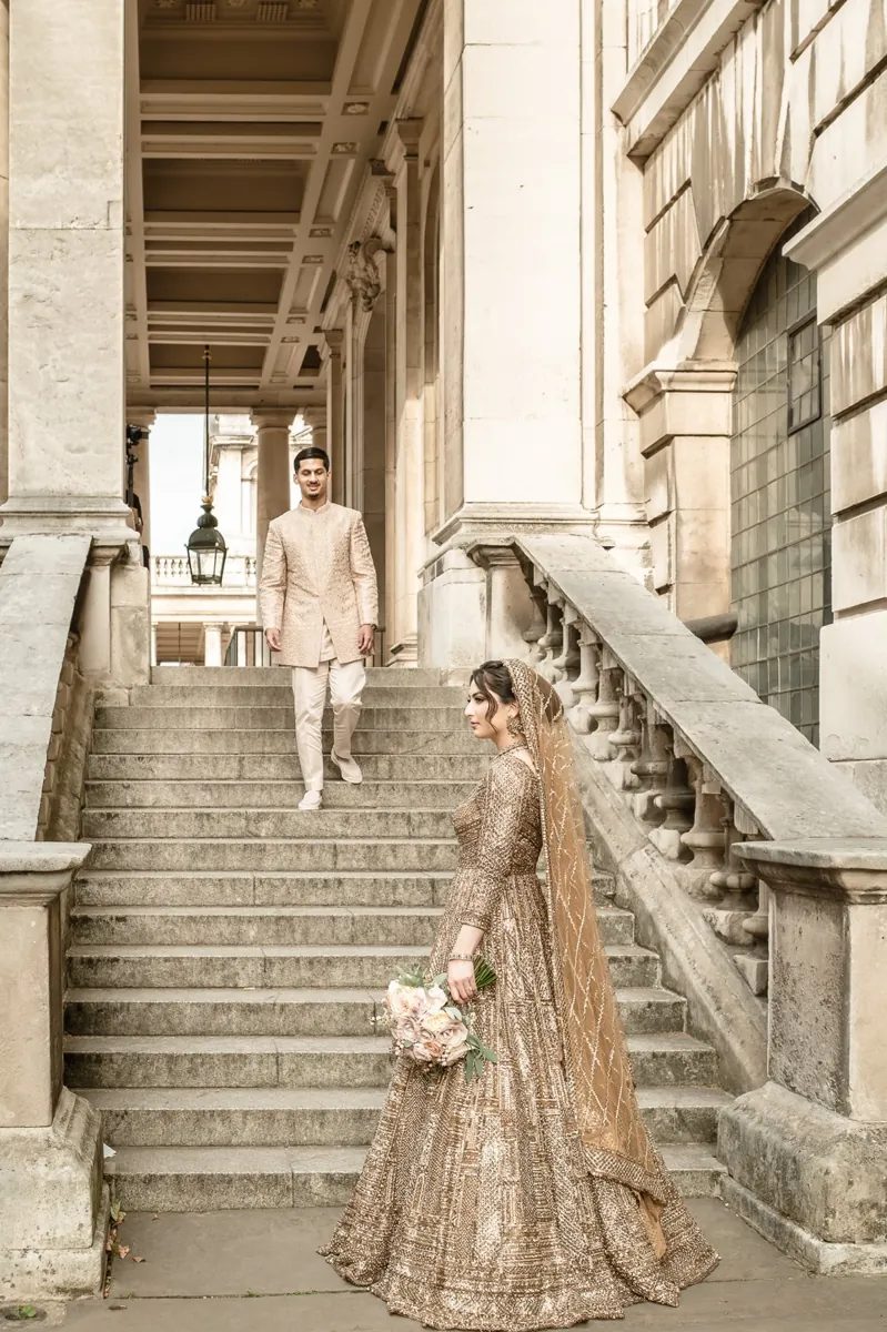 Bride holding a bouquet at the foot of stone steps as the groom walks down towards her