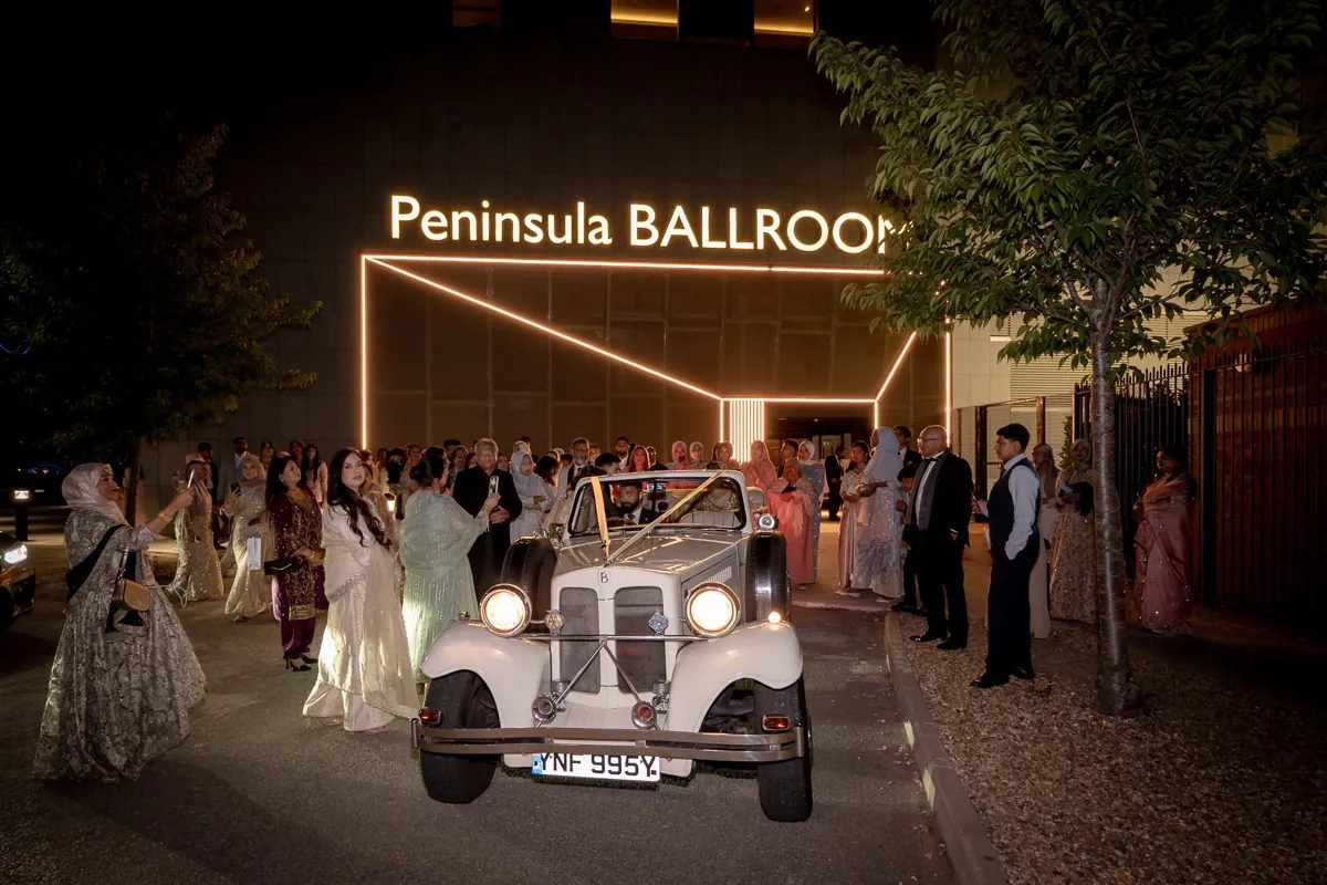 Guests gathered around the vintage wedding car outside the Peninsula Ballroom at night
